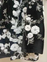 نمای نزدیک از گل‌دوزی سفید و ملیله طلایی روی کت مخمل مشکی